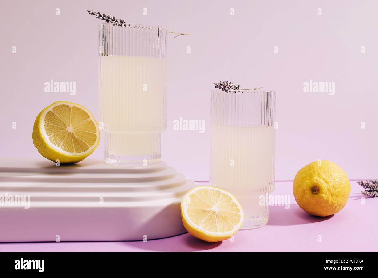 Lavender lemonade in ribbed glasses and lemons on purple background