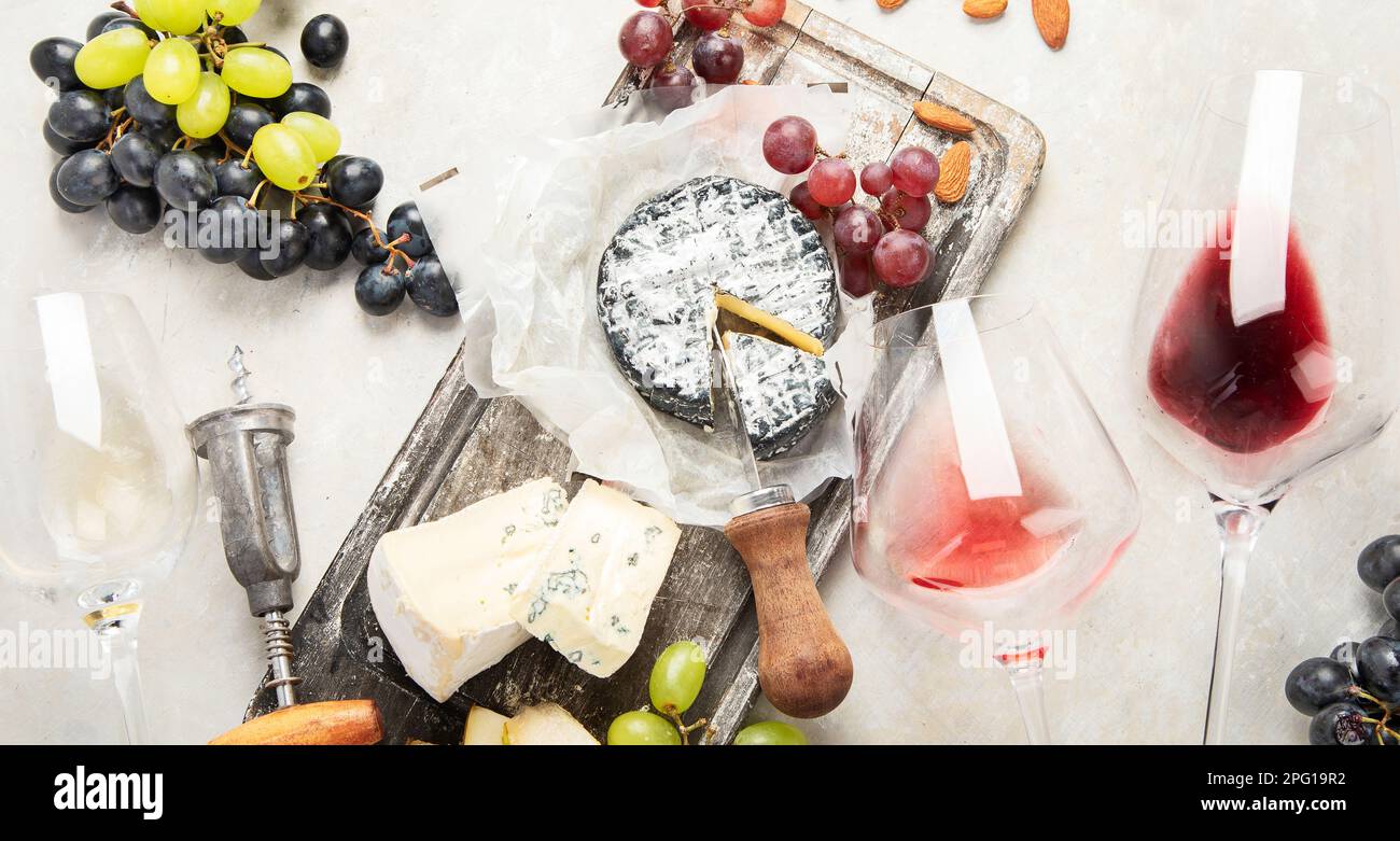 Pink and red wine served with cheeses, nuts, grapes and glasses of wine. Delicious food wine snacks assorted served on boards. Flat lay on a white  ba Stock Photo