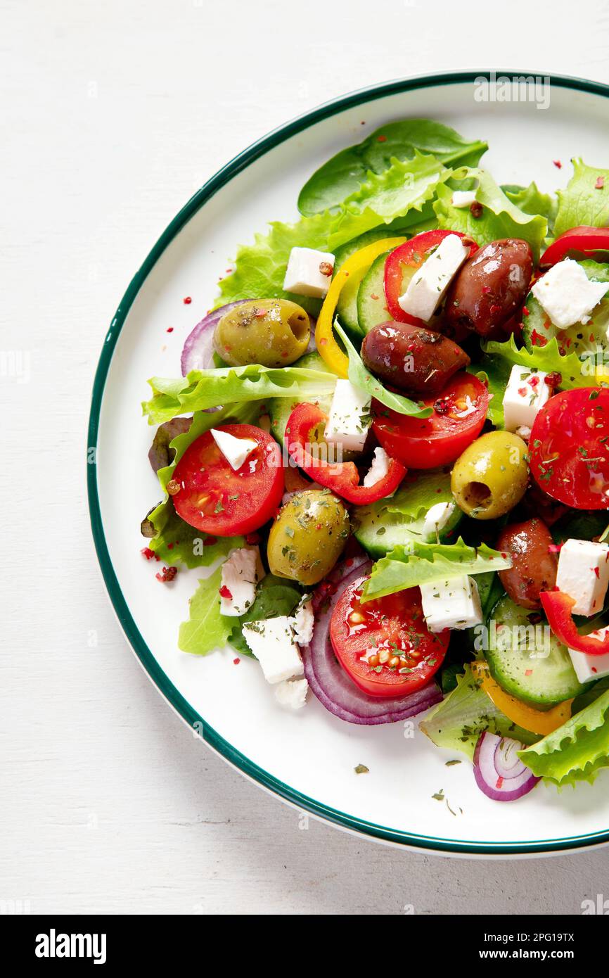 Greek salad of fresh cucumber, tomato, sweet pepper, lettuce, red onion, feta cheese and olives with olive oil on a white background. Healthy food, to Stock Photo