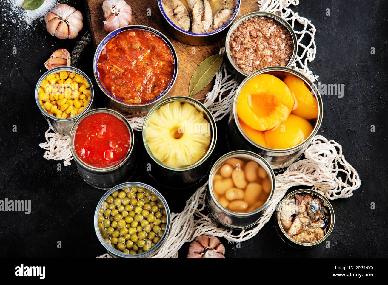 Various canned vegetables, meat, fish and fruits in tin cans. On a dark background. Top view. Stock Photo