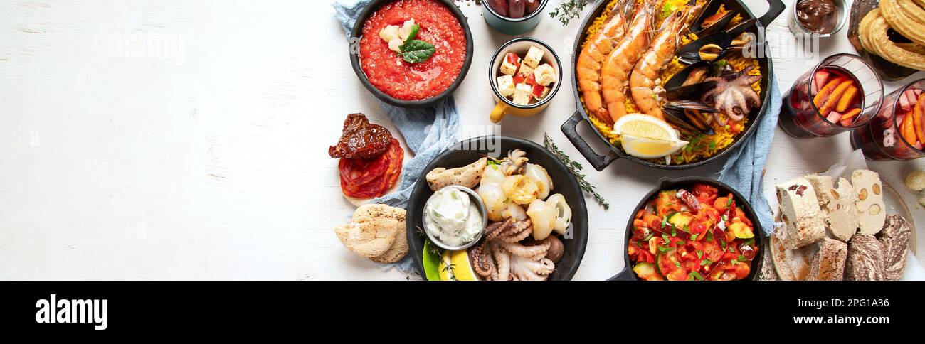 Typical spanish tapas concept. Concept include jamon, chorizo sausage, brushettas, bowl with olives, shrimp, pan with paella, cheese, sangria, churros Stock Photo