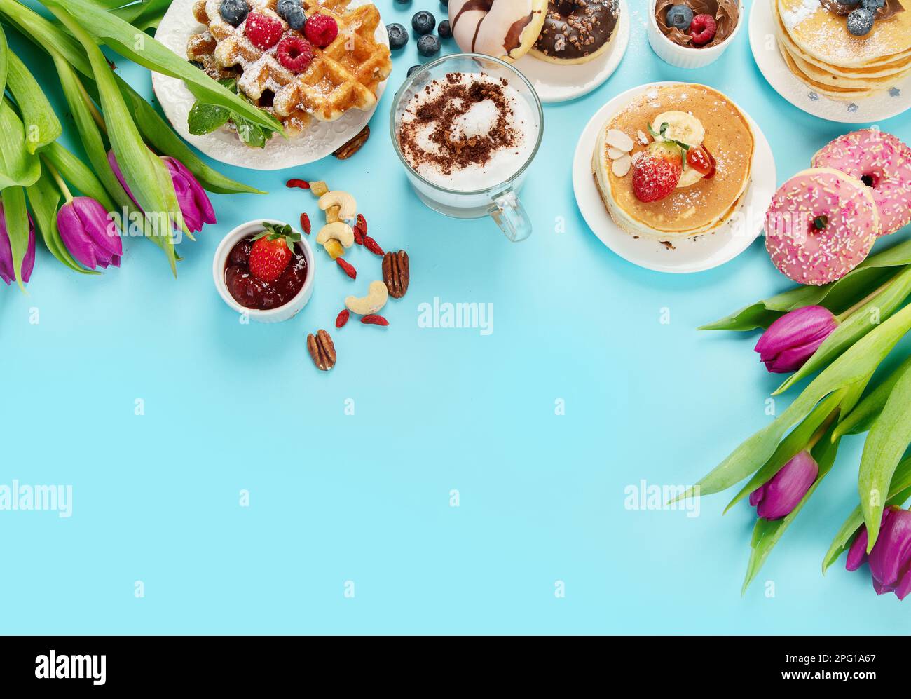 Summer or spring breakfast with Cup of hot cappuccino coffee,  pancakes, waffles coffee, tulips  flowers, craft envelope on blue background.  Top view Stock Photo