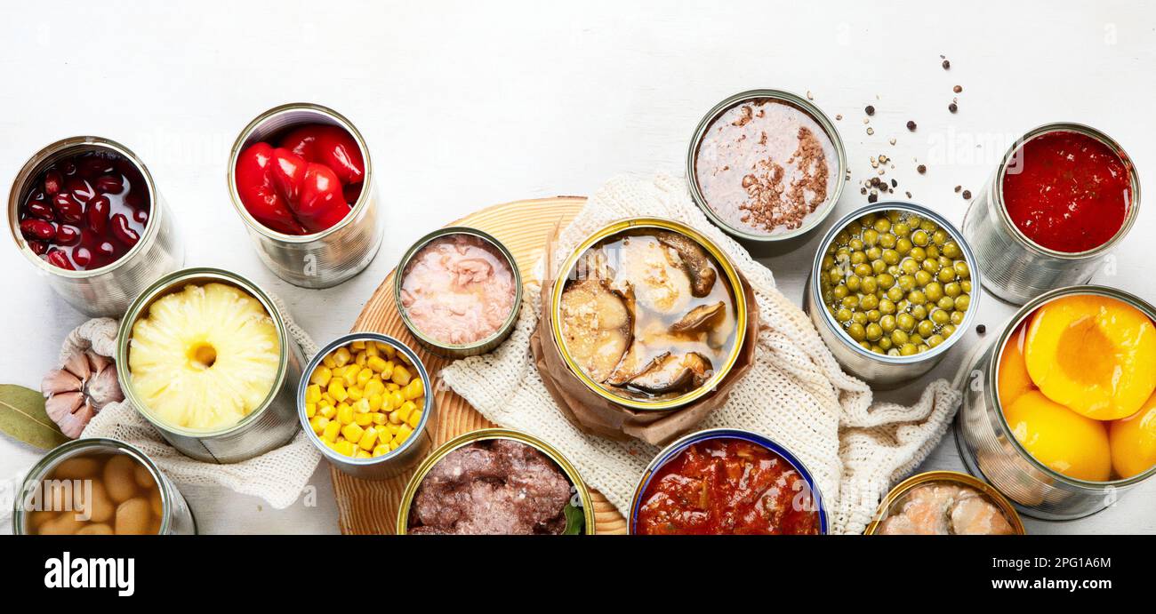 Various canned vegetables, meat, fish and fruits in tin cans. On a white background. Top view. Panorama with copy space. Stock Photo