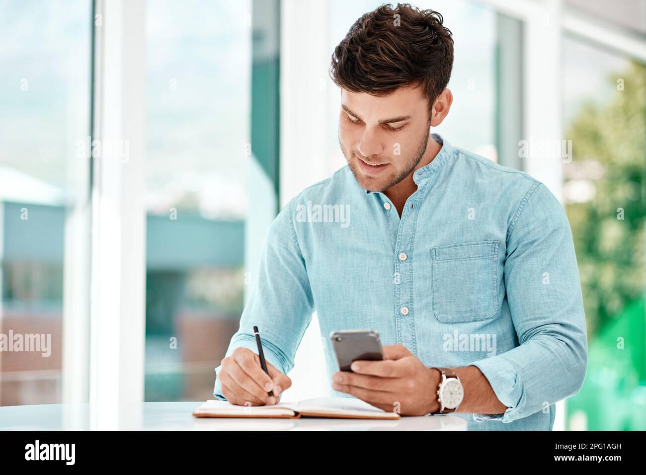 Making notes helps him improve. a handsome young businessman making notes while siting at a table in his office. Stock Photo