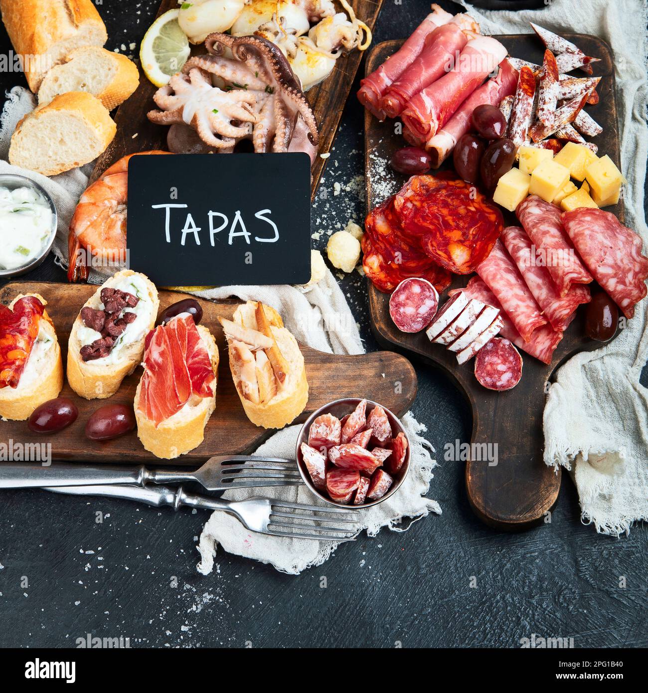 Typical spanish tapas with jamon slices, chorizo, salami,  olives,  potatoes snack Patatas bravas, seafoods on dark table. Traditional spanish food. T Stock Photo