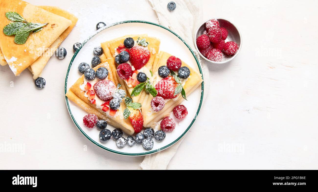 Healthy breakfast, homemade traditional crepes or pancakes with fresh berries, morning light background. Copy space top view Stock Photo