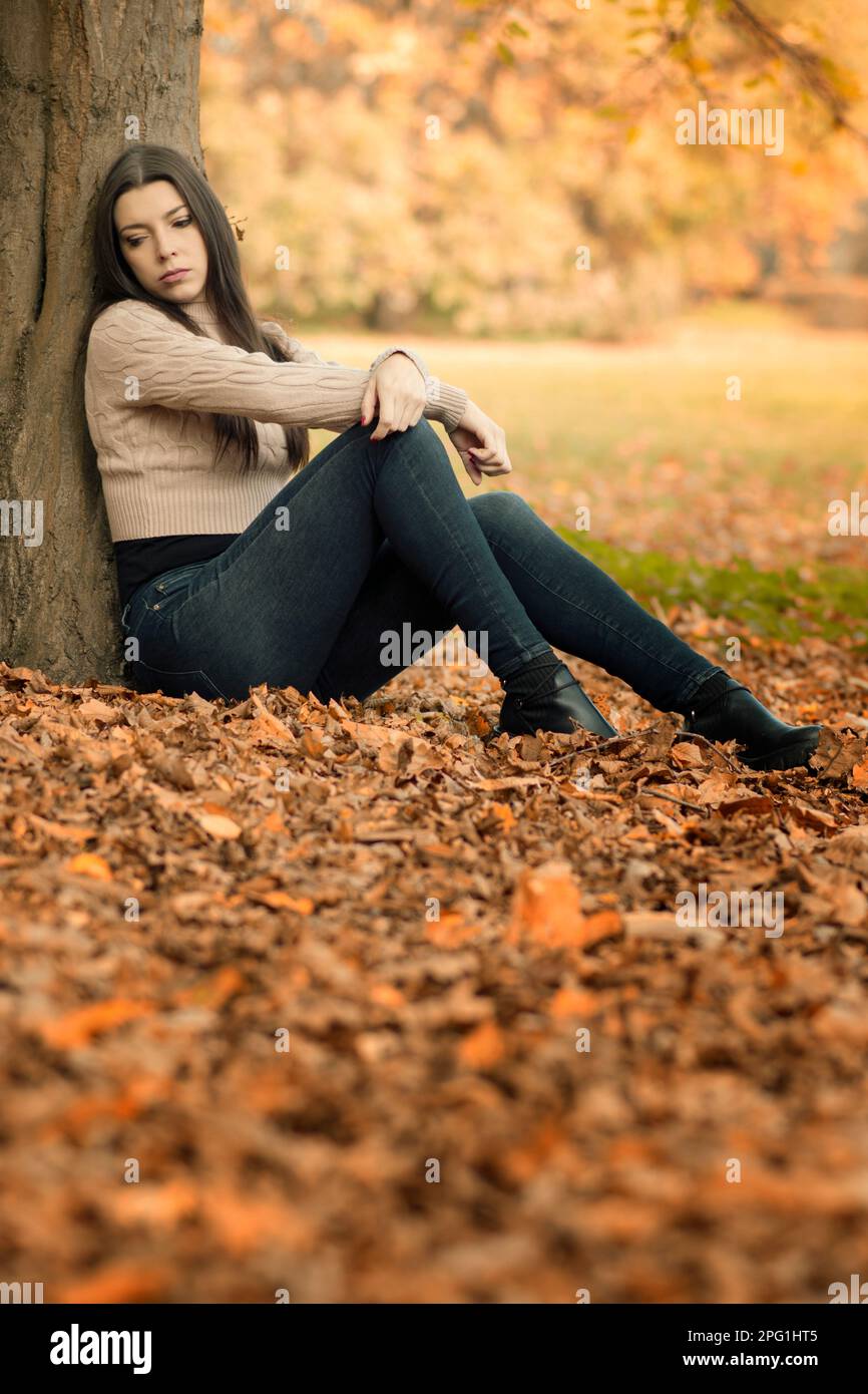 Sad beautiful woman sat by the tree looking away Stock Photo