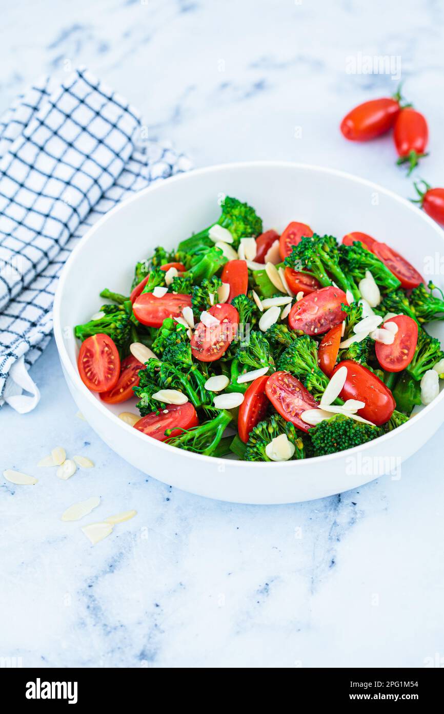 Broccoli salad with cherry tomatoes and almonds in a white bowl. Vegan detox recipe. Stock Photo