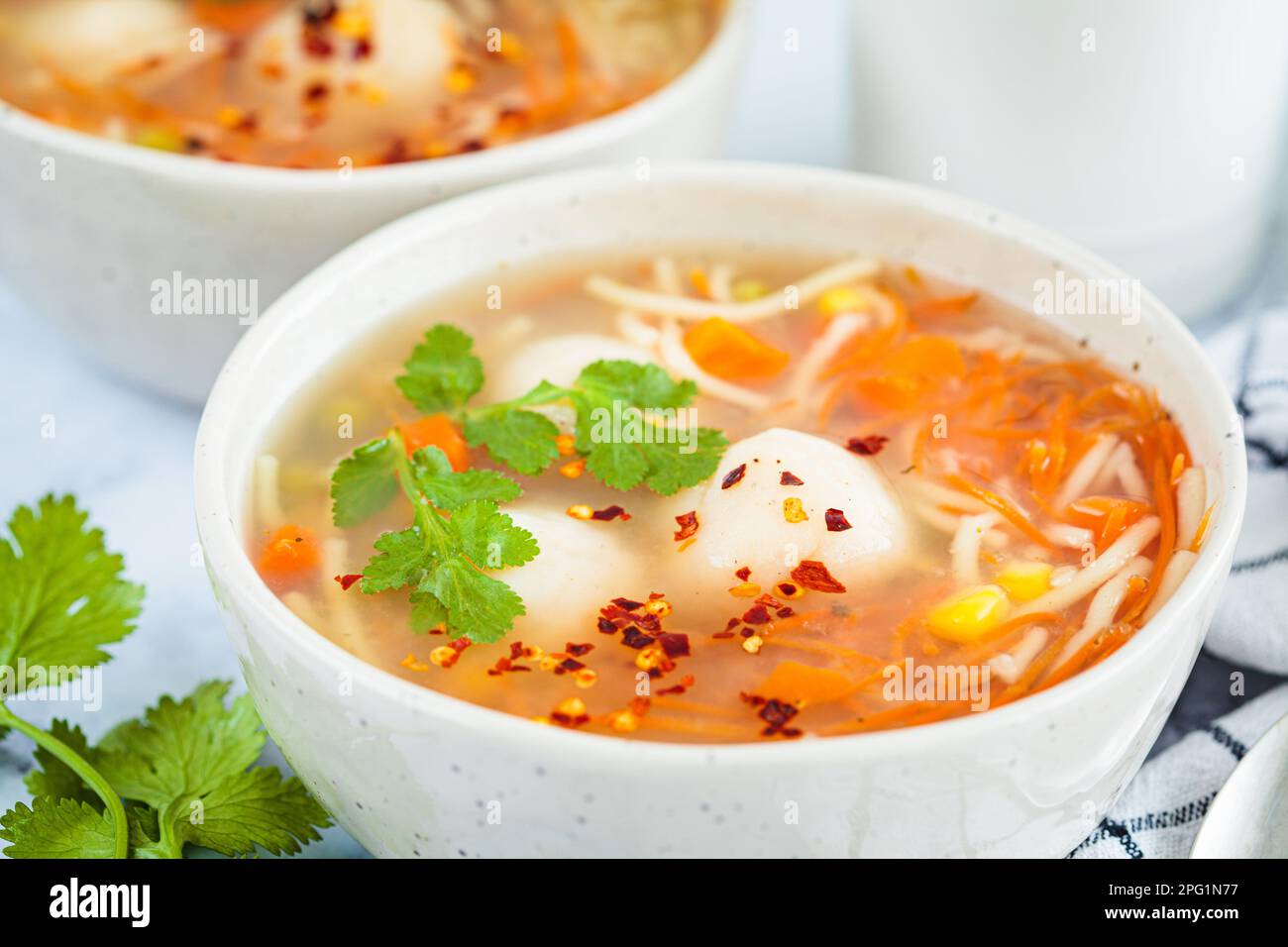 Potato balls soup with noodles and vegetables in a white bowl, white background, close-up. Vegan food concept. Stock Photo