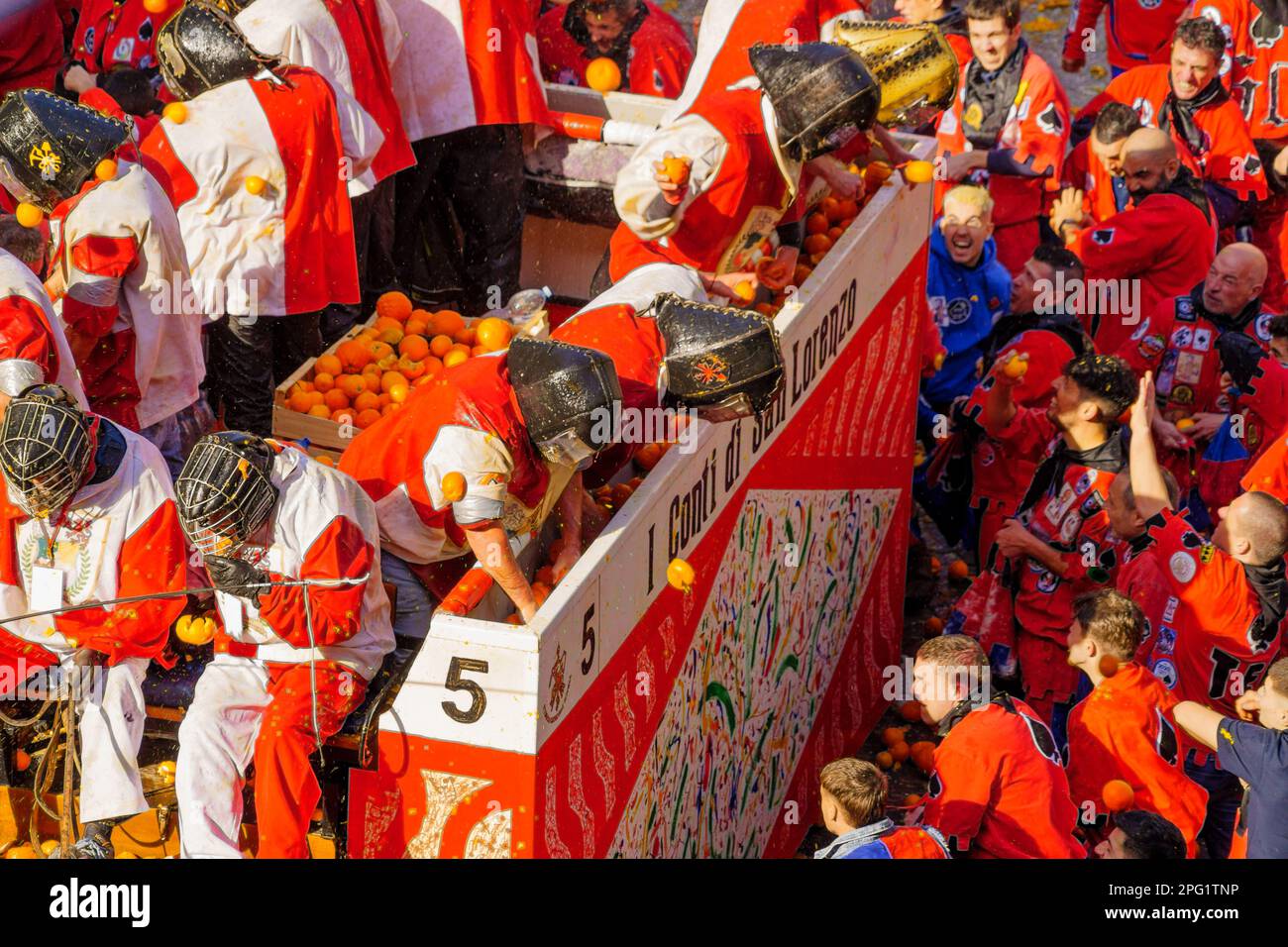 Ivrea, Italy - February 19, 2023: Groups in traditional dressings, and crowd with red hats, take part in the Battle of the Oranges, part of the histor Stock Photo