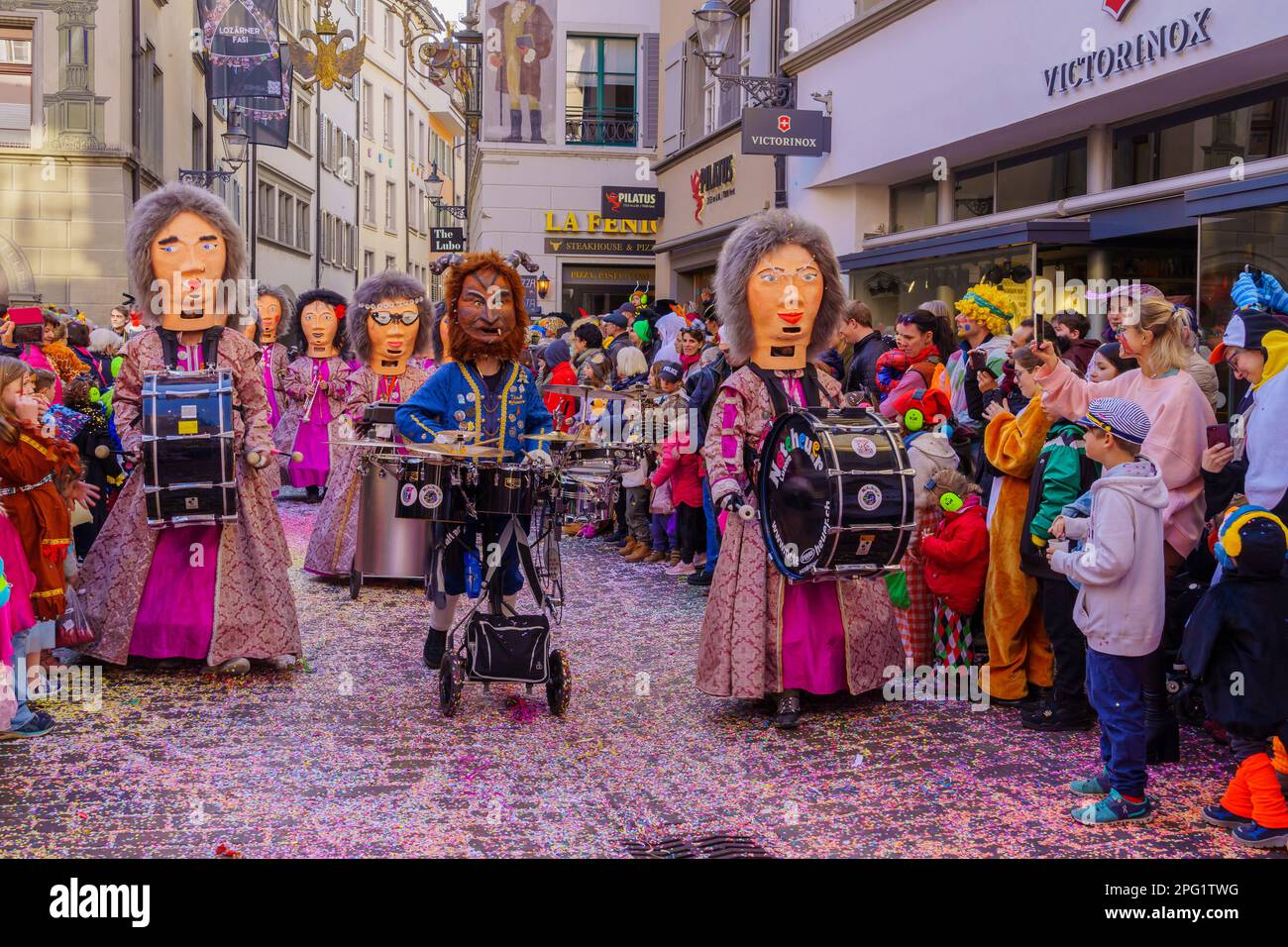 Lucerne, Switzerland - February 21, 2023: Group of participants in costumes march in the streets, and crowd, part of the children parade of the Fasnac Stock Photo