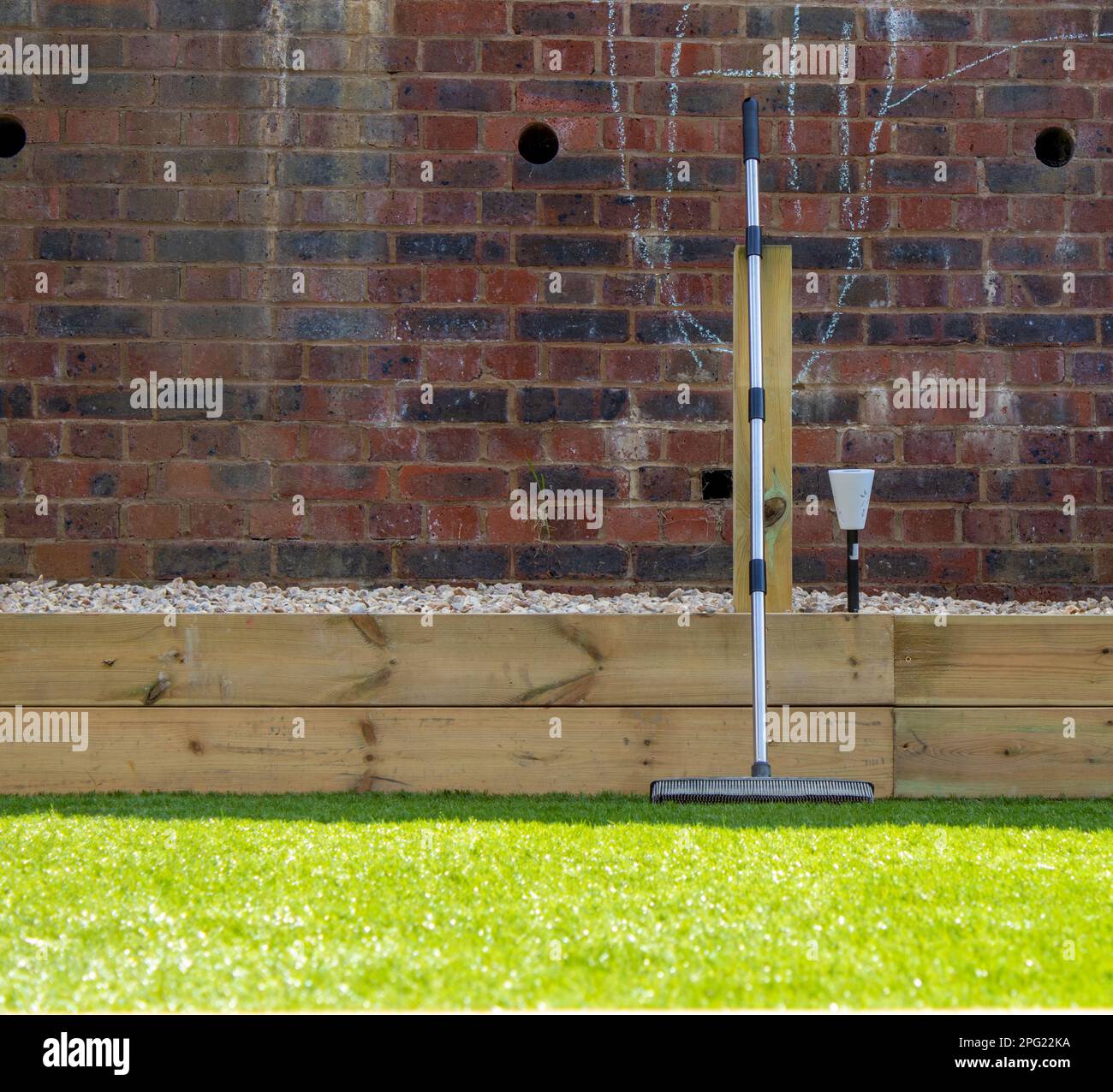 Rubber broom leaning on artificial grass in front of brick wall in a