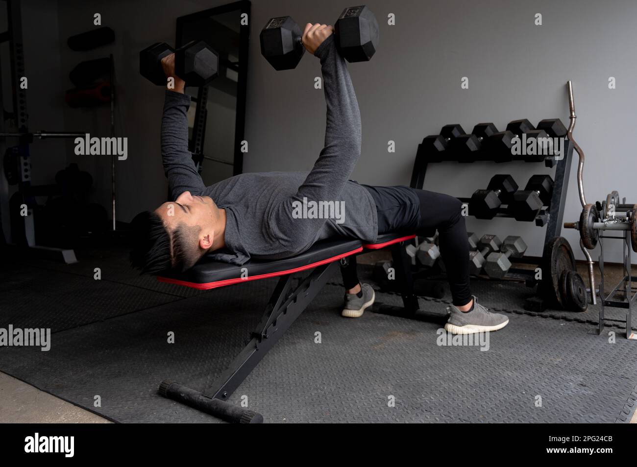 Young Man Bench Pressing Dumbbells at In Home Garage Gym Stock Photo