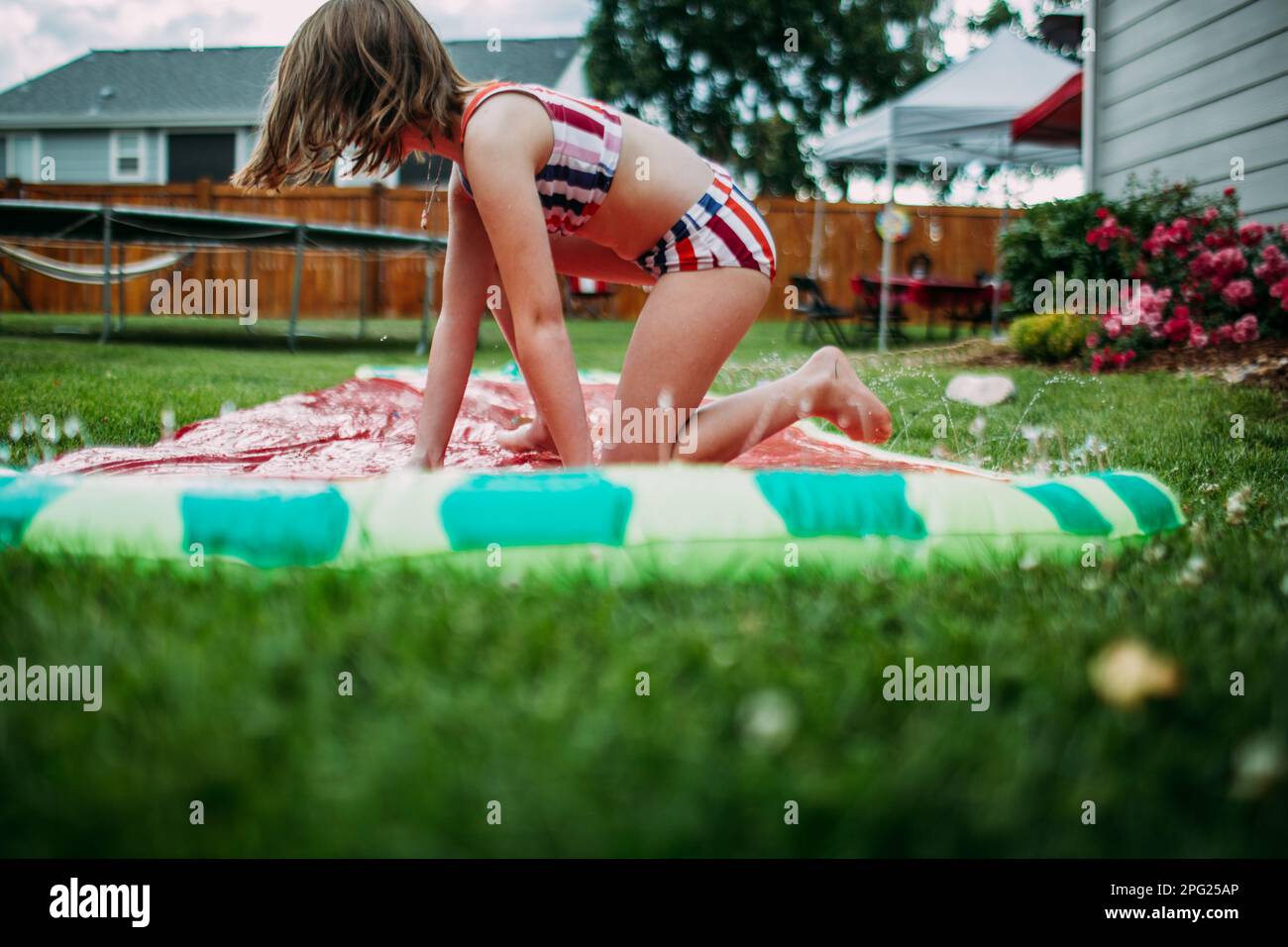 Young girl getting off slip and slide in back yard Stock Photo