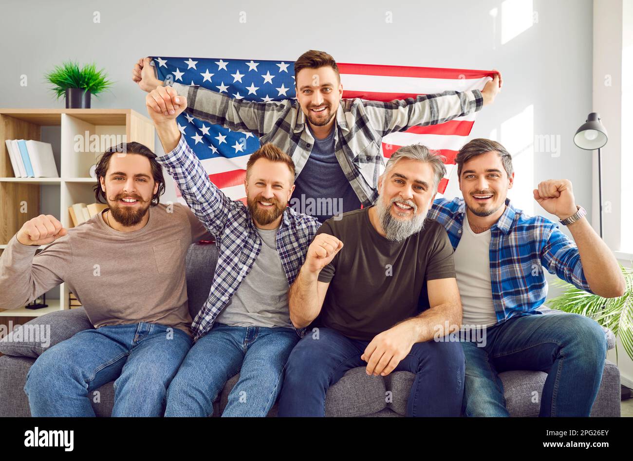Group of Americans with flag sitting on sofa and watching soccer match on television Stock Photo