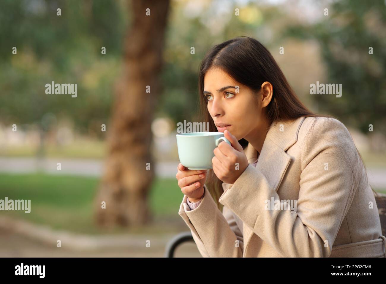 Woman drinking coffee looks away at sunset in a park in winter Stock Photo