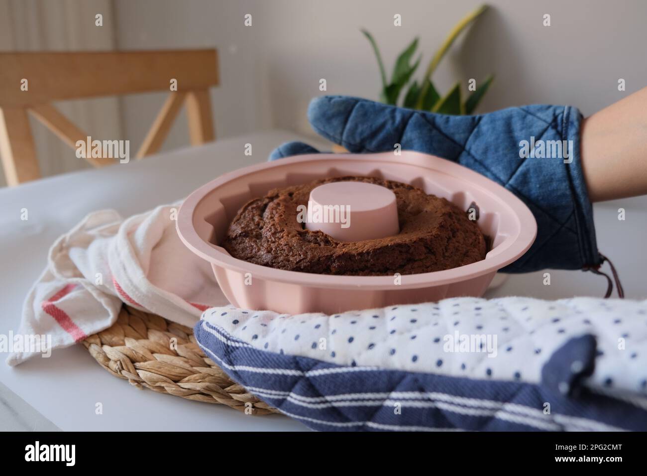 Baked cake, baked cake in a pink round silicone mold between two hands on a white kitchen cloth and placemat in the kitchen. The concept photo. Stock Photo