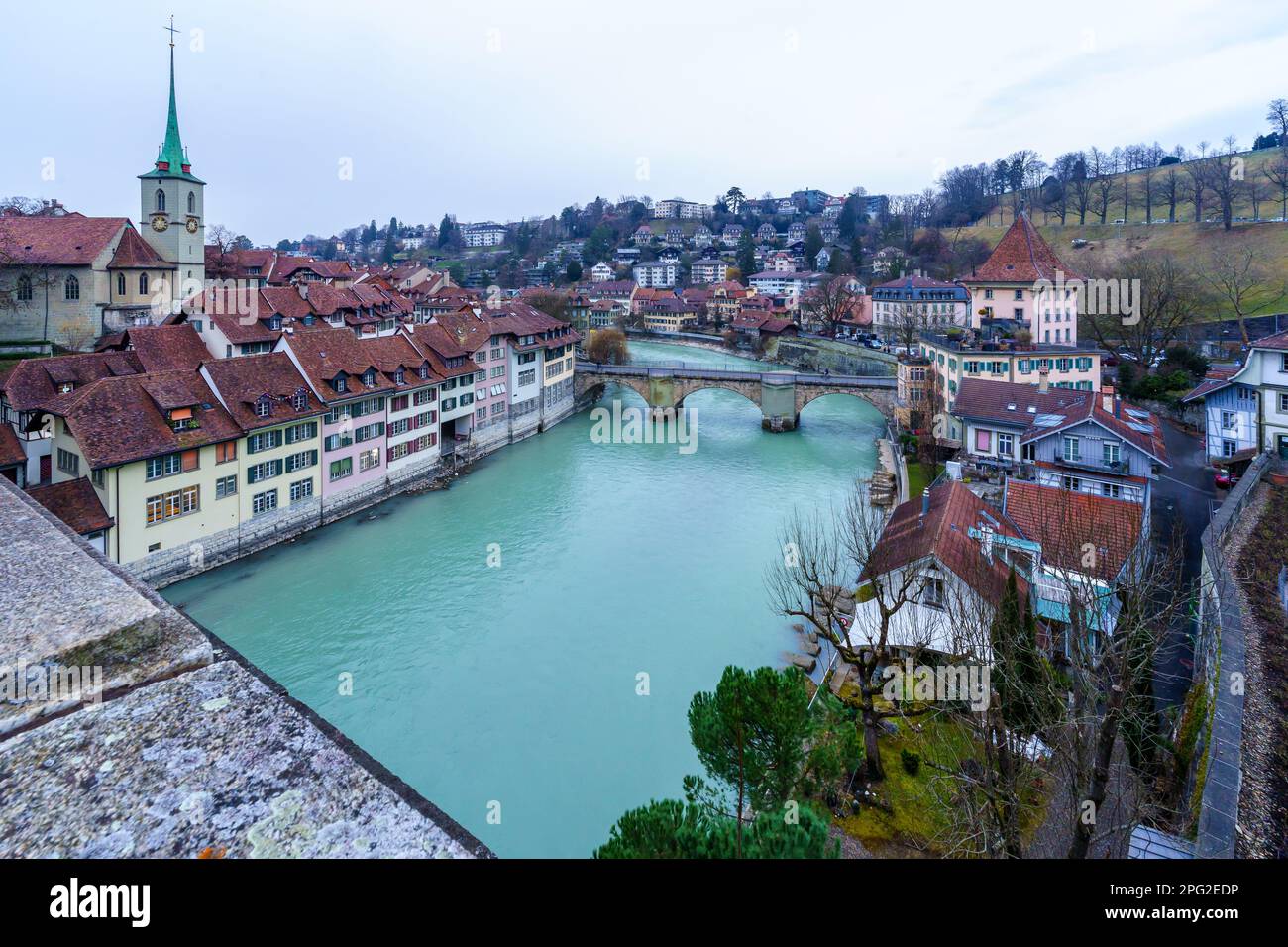 View of the Aare River, Nydeggkirche church, Untertorbrucke bridge, with various buildings, locals, and visitors, in Bern, Switzerland Stock Photo