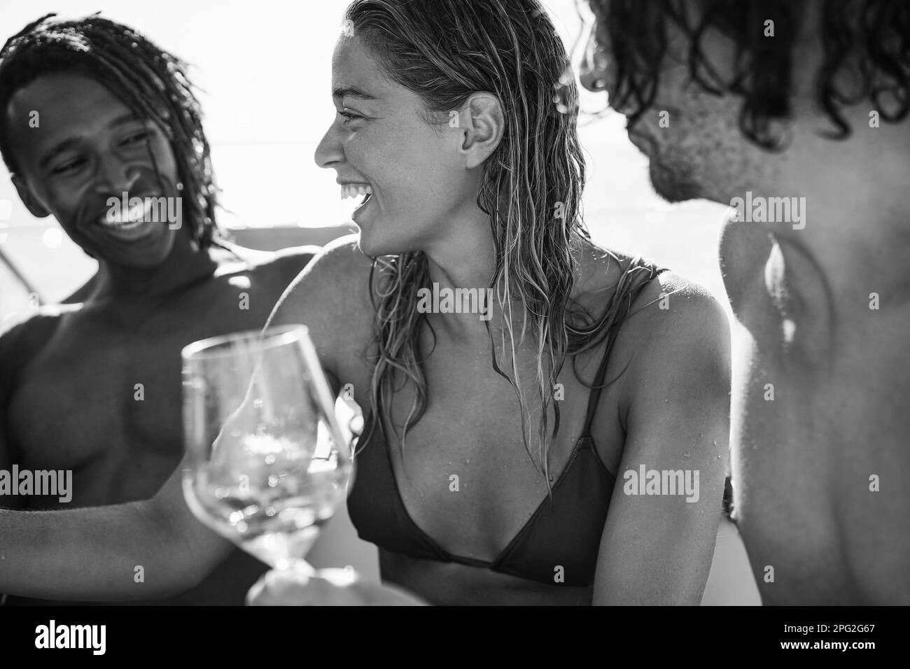 Happy multiracial friends having fun drinking champagne at boat party outdoor - Focus on center girl face - Black and white editing Stock Photo