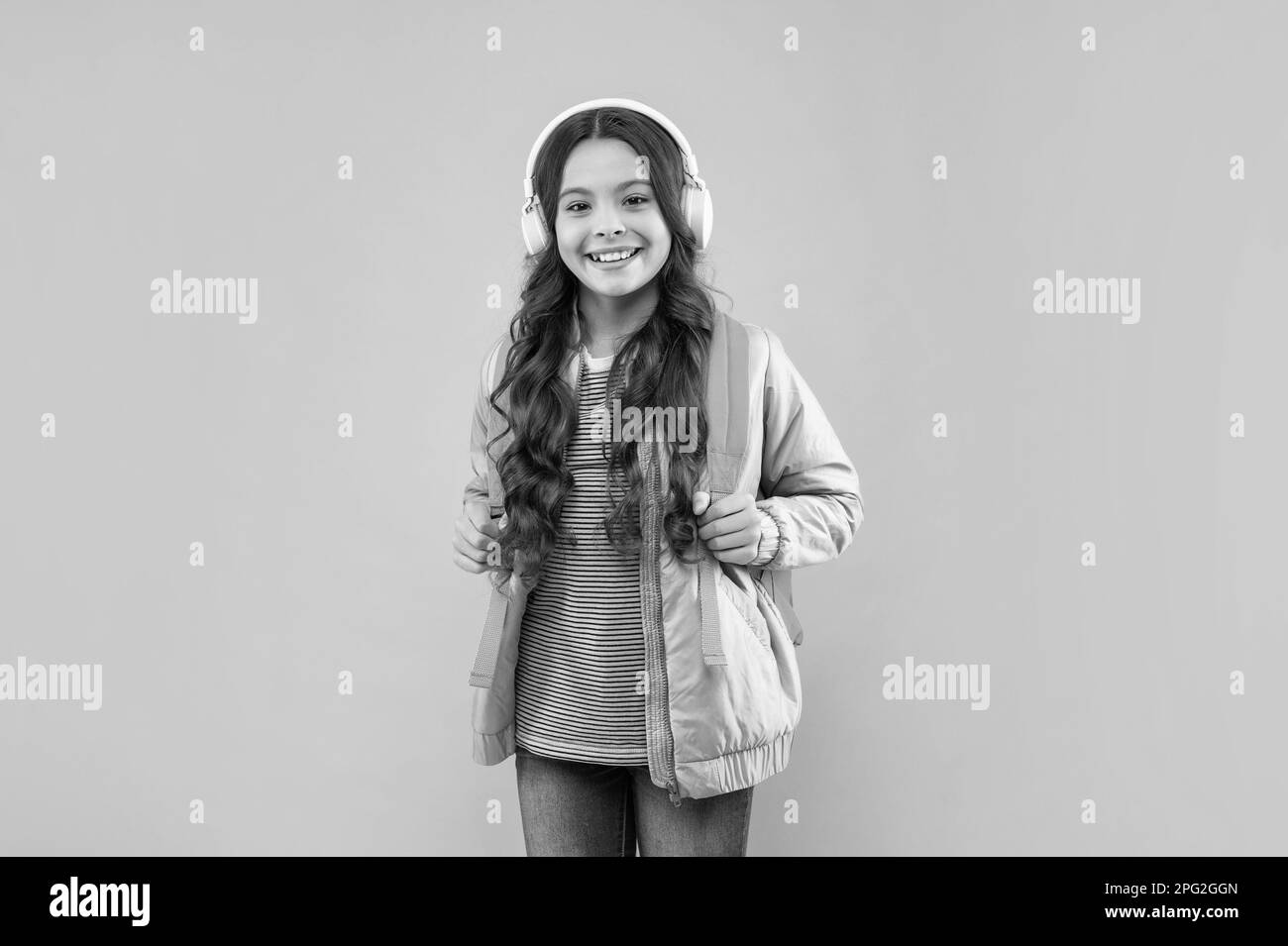 happy child listen music in headphones and carry backpack on pink