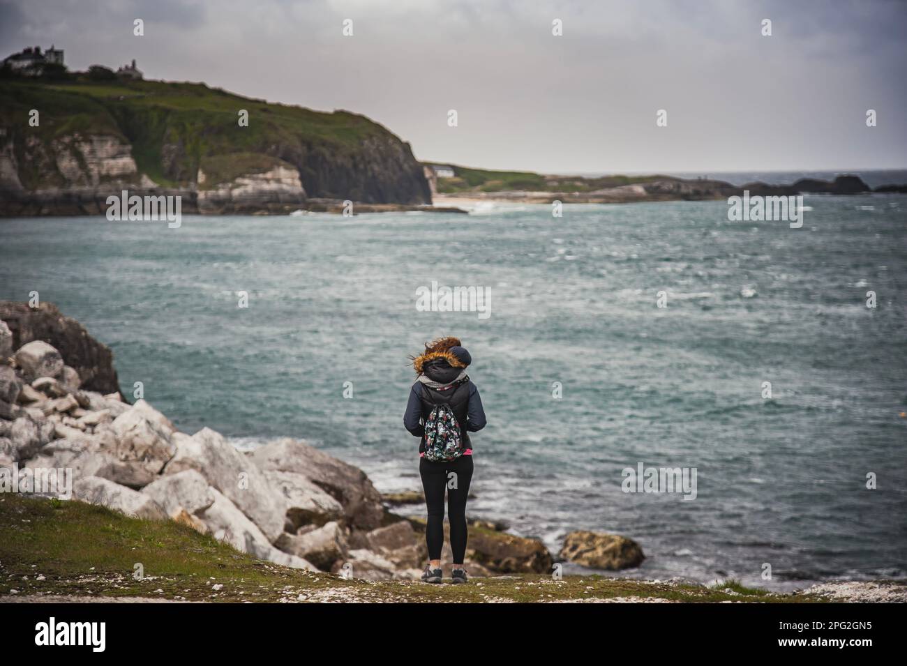 Girl taking a break to admire the dramatic cliffs and Irish gloomy landscape by the Giant's Causeway. Woman meditating or contemplating by the ocean Stock Photo