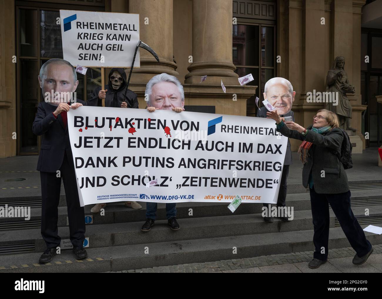 20 March 2023, Hesse, Frankfurt/Main: Activists protest against the IPO of the arms company Rheinmetall in front of the stock exchange in Frankfurt with a placard reading 'Rheinmetall blood shares now finally on the DAX thanks to Putin's war of aggression and Scholz's turnaround'. One demonstrator is wearing a mask with the likeness of Armin Papperger, Rheinmetall's CEO, while two others symbolize German Chancellor Olaf Scholz and Russian President Putin. Photo: Boris Roessler/dpa Stock Photo