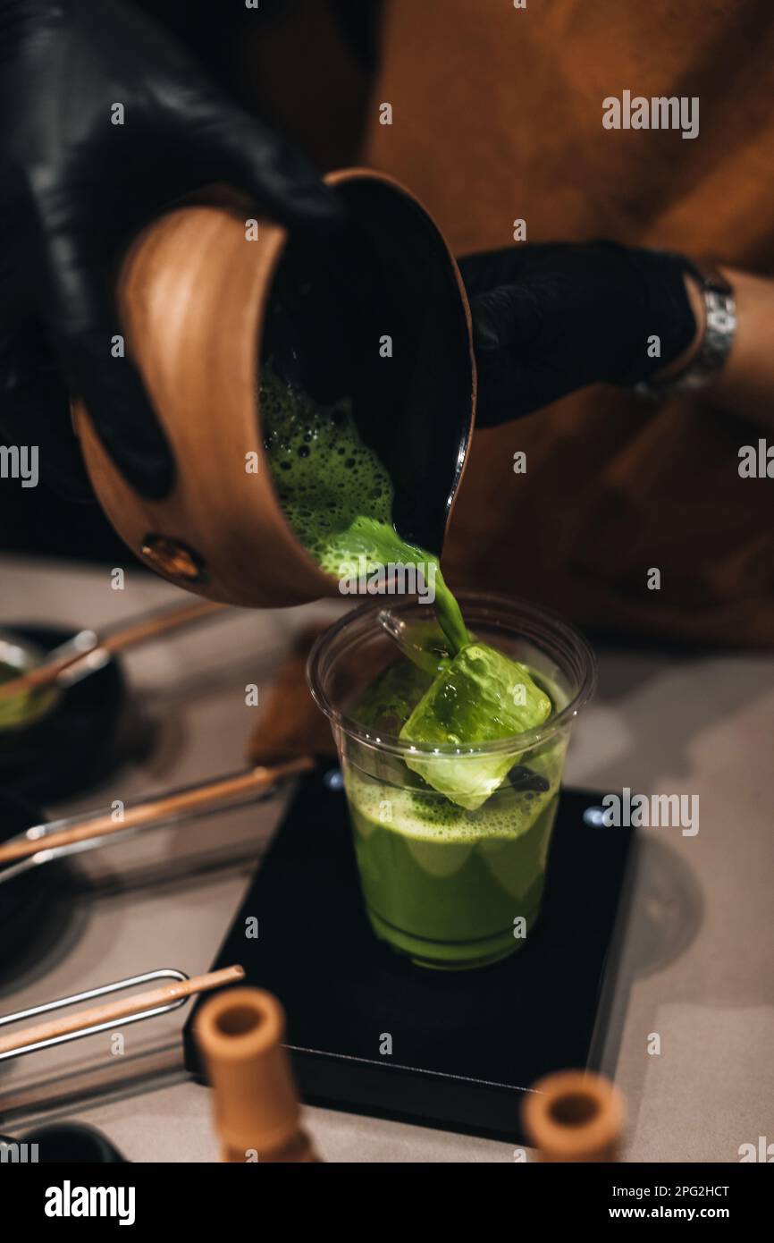 Matcha Japanese green tea making process. Female hands pouring matcha into a plastic glass. Traditional organic utensils. Stock Photo