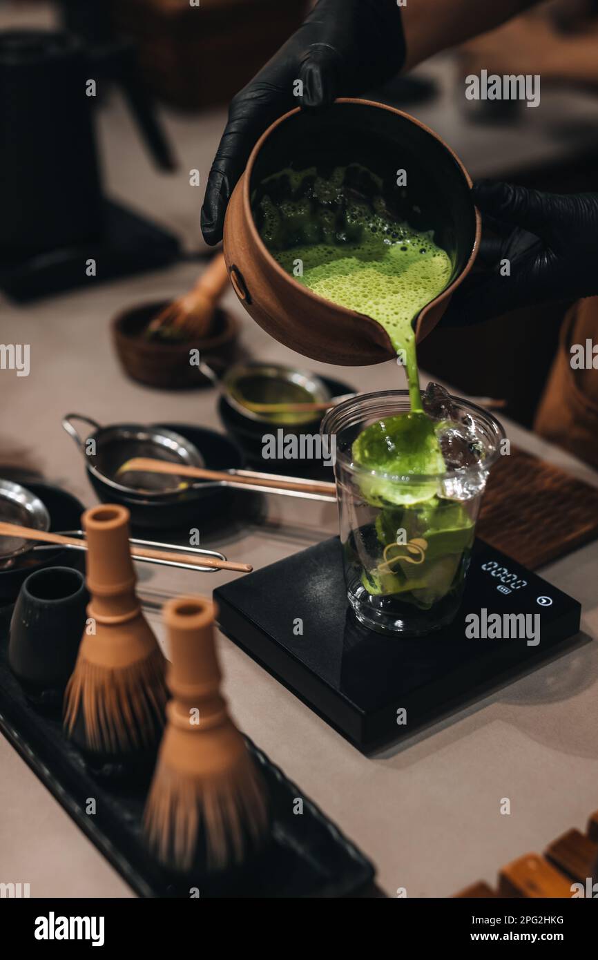Matcha Japanese green tea making process. Female hands pouring matcha into a plastic glass
