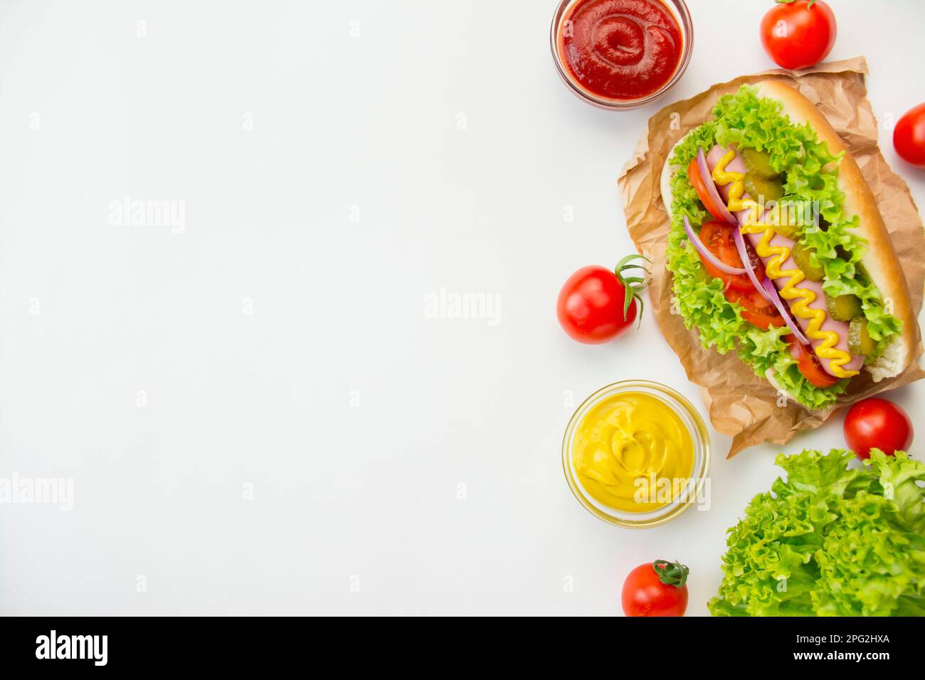 Hot dog with pickles, tomatoes and lettuce on a white background. Fast