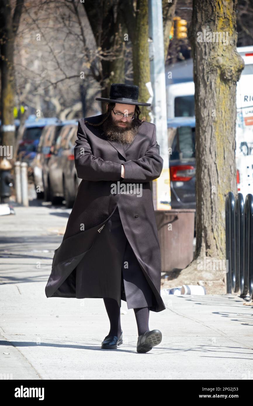 A Hasidic jewish man in a long coat with high black stockings walks on Bedford Avenue on a cold winter say. Hands inside sleeves is a familiar pose. Stock Photo