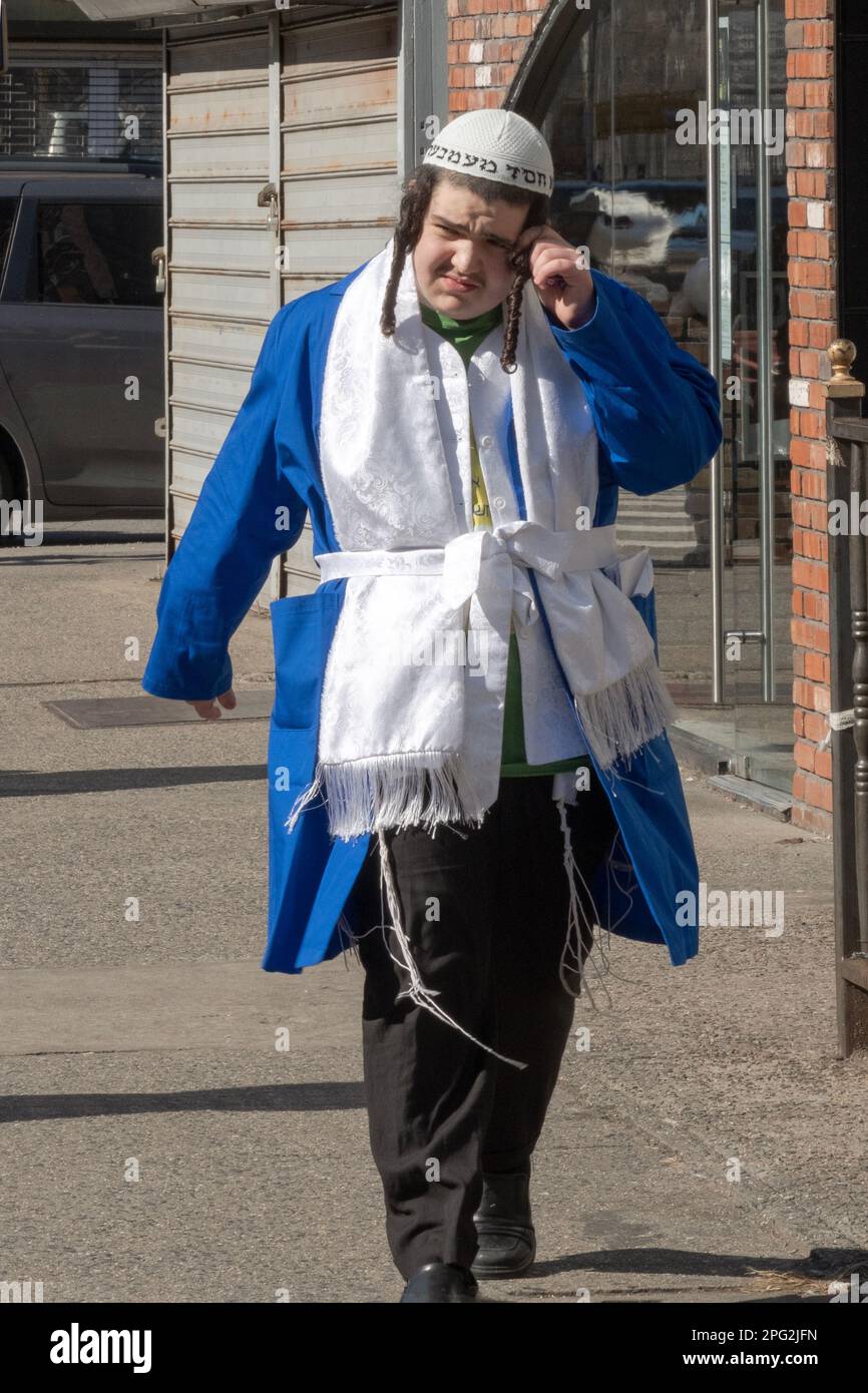 A young man in his colorful Purim costume twirls his peyus. On Lee Ave. In Brooklyn, New York City. Stock Photo