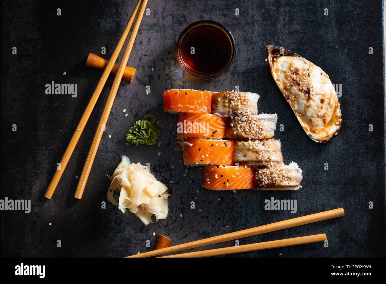 Sushi, rolls and baked mussels on a dark background with Chinese chopsticks top view. Healthy seafood with sauce and ginger. Chinese food. Stock Photo
