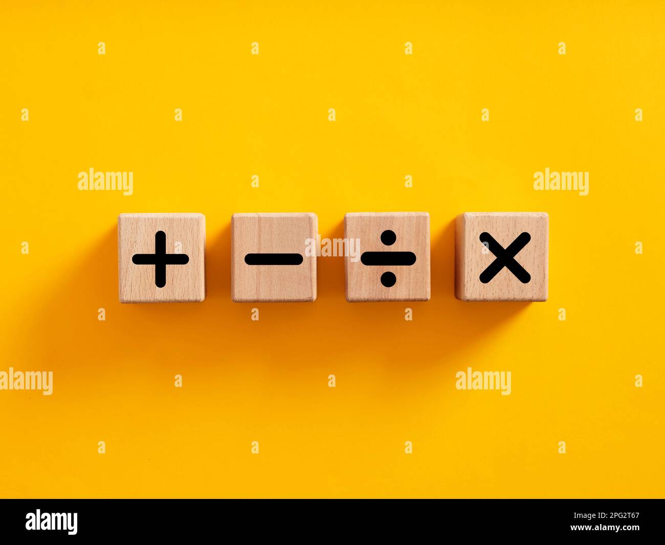 Basic mathematical operations symbols. Plus, minus, multiply and divide symbols on wooden cubes on yellow background. Mathematic or math education and Stock Photo