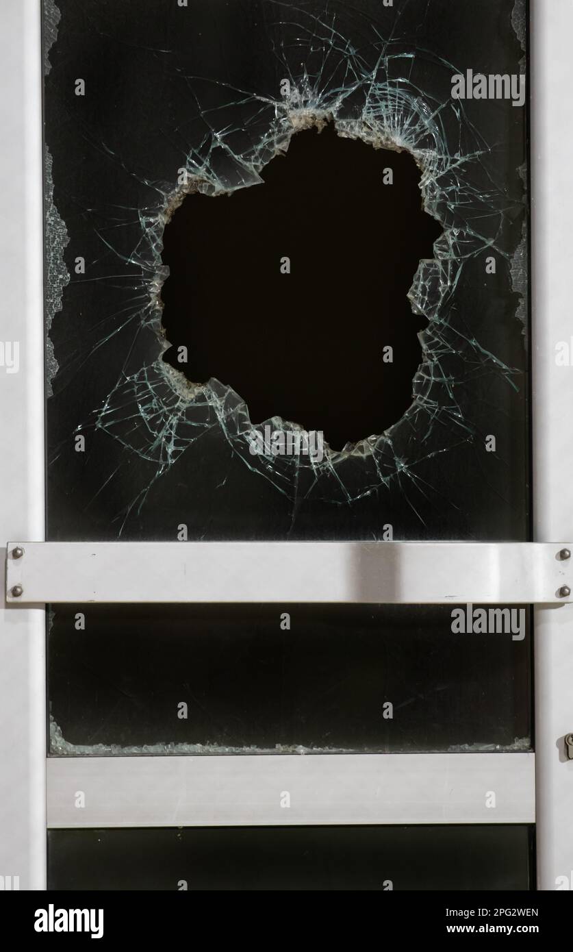 a bullet hole in glass is a real bullet hole of a large caliber projectile bullet. Glass door pierced by a bullet during the war, terrorist attack. Br Stock Photo