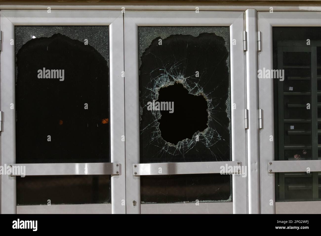 a bullet hole in glass is a real bullet hole of a large caliber projectile bullet. Glass door pierced by a bullet during the war, terrorist attack. Br Stock Photo