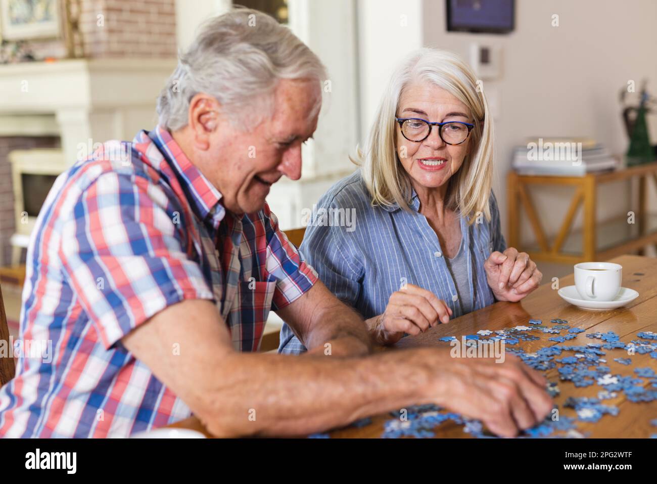 Happy caucasian senior friends sitting at table doing jigsaw puzzle together Stock Photo