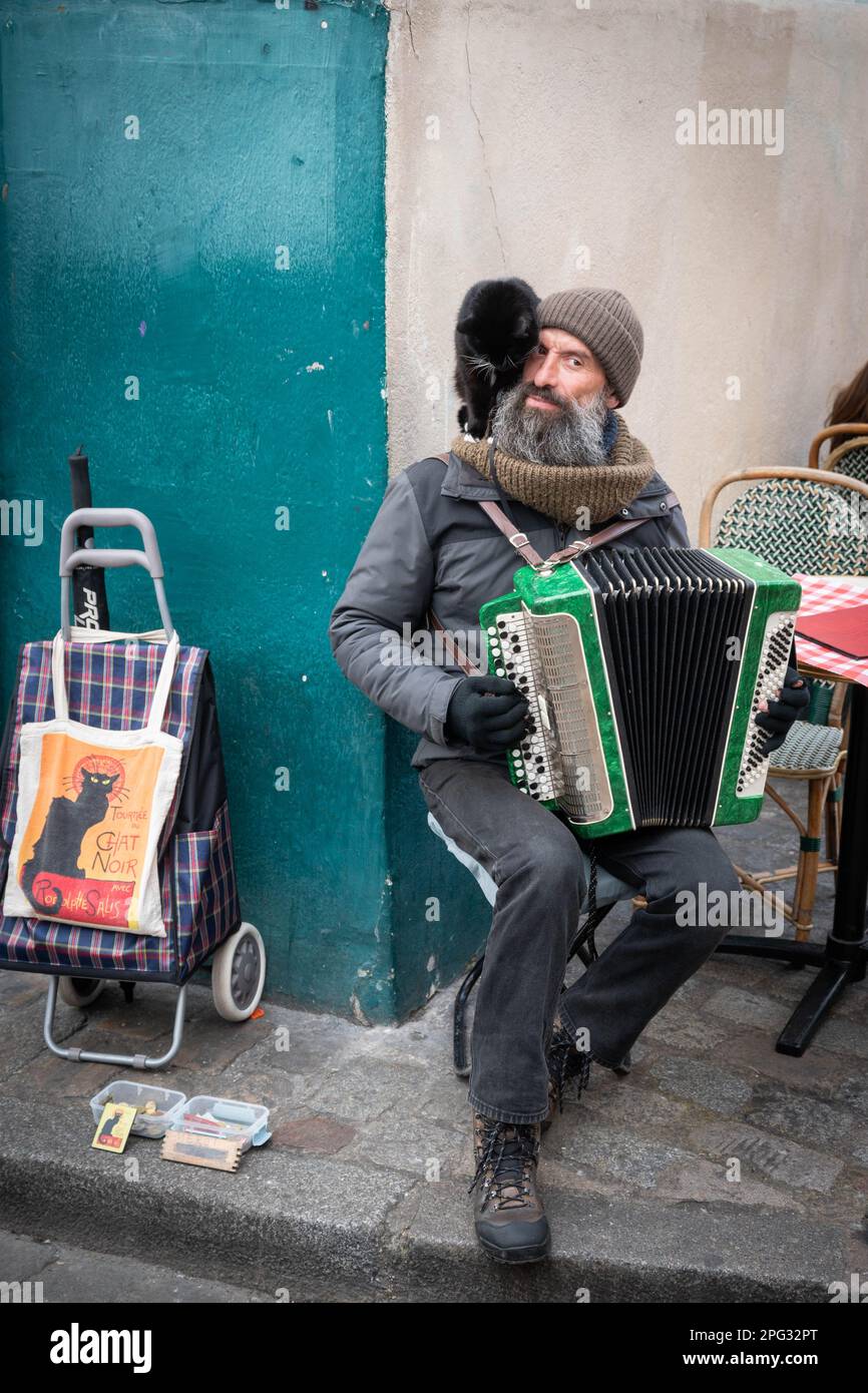 Parisian French busker with accordion with a black cat on his shoulder and 'chat noir' bag, plays in the Place du Tertre artists square in Montmartre Stock Photo