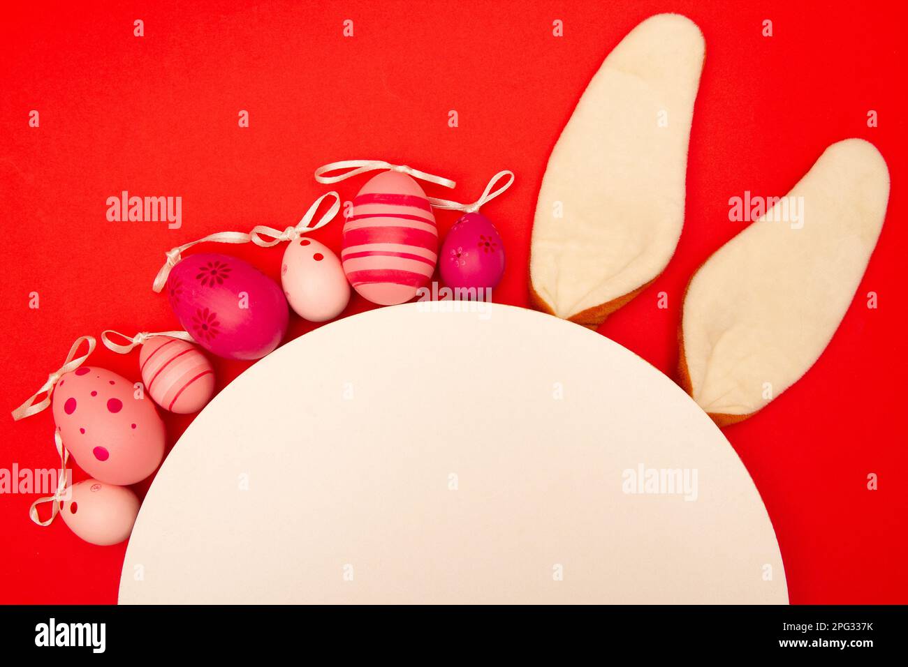 Easter eggs, white circle, and bunny ears decorate a red background Stock Photo