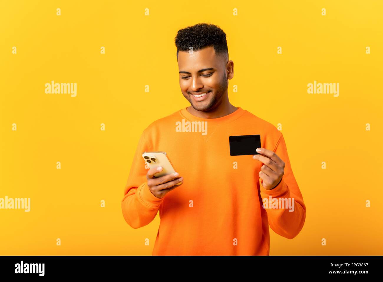 Carefree happy Indian man holding credit card and smartphone, looking ...