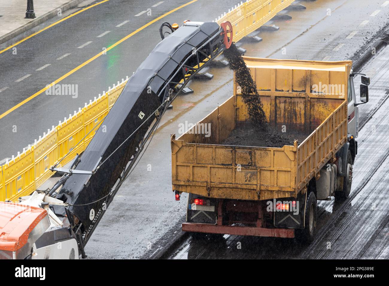 Milling machine working and removing asphalt from the road and pouring