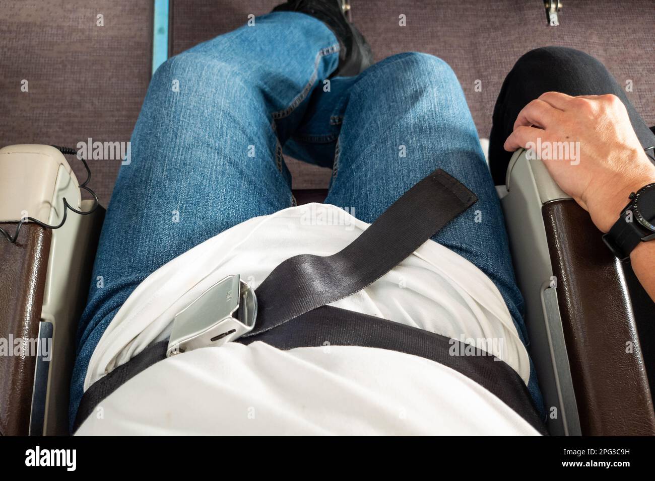 Passenger with fastened seat belt seated on aircraft seat for safety Stock Photo