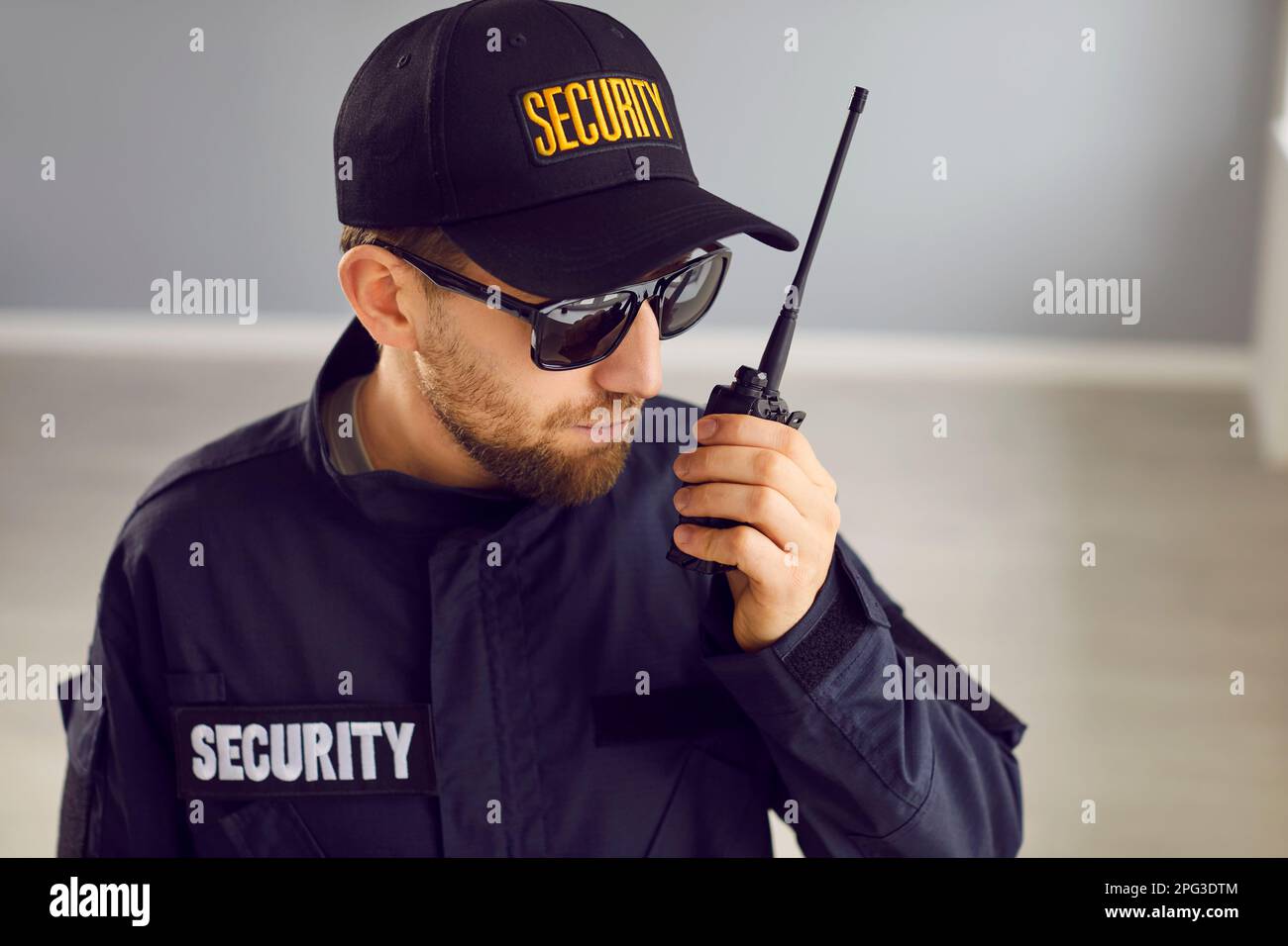 Young male security guard worker in black uniform monitoring house and using radio Stock Photo