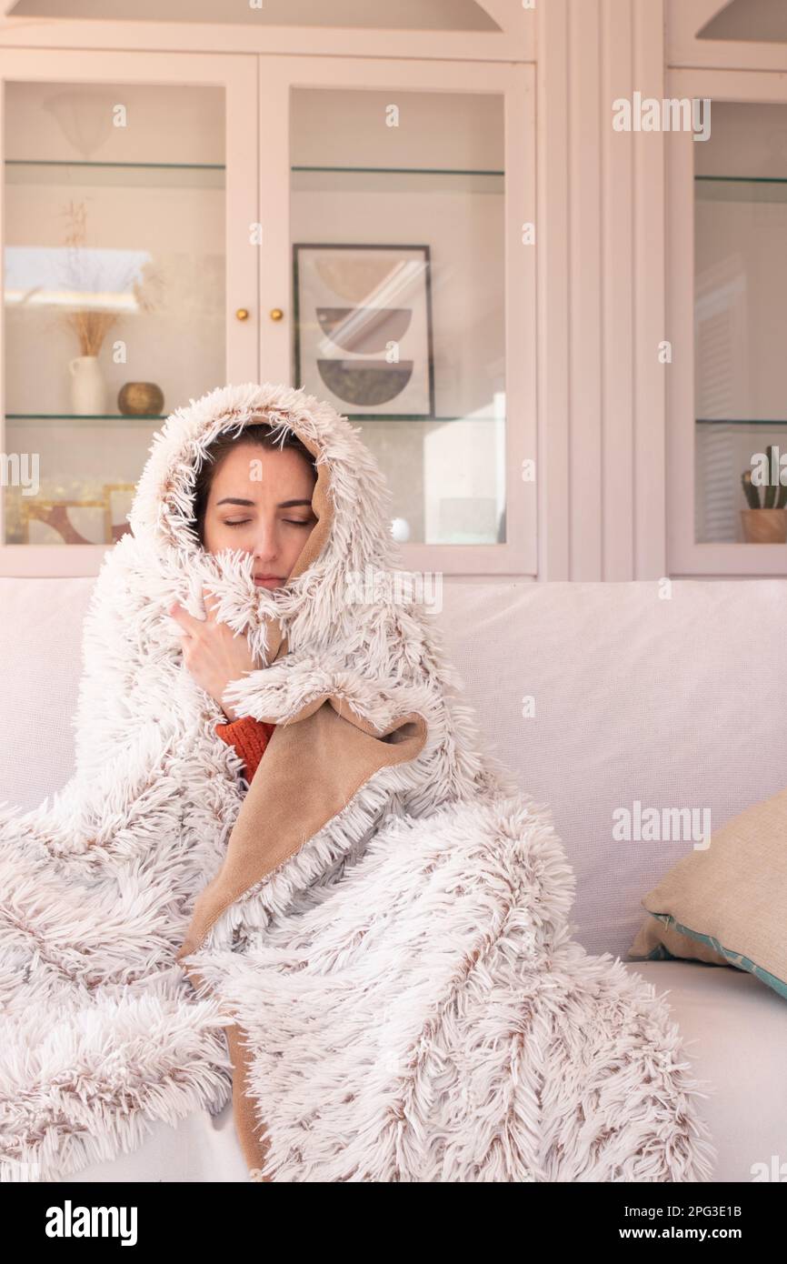 Ill female with fever freezing under fuzzy plaid while resting on comfortable sofa in modern living room with closed eyes Stock Photo