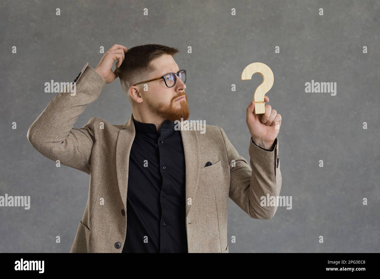 Puzzled man holding question mark, scratching head and thinking of answer to difficult question Stock Photo