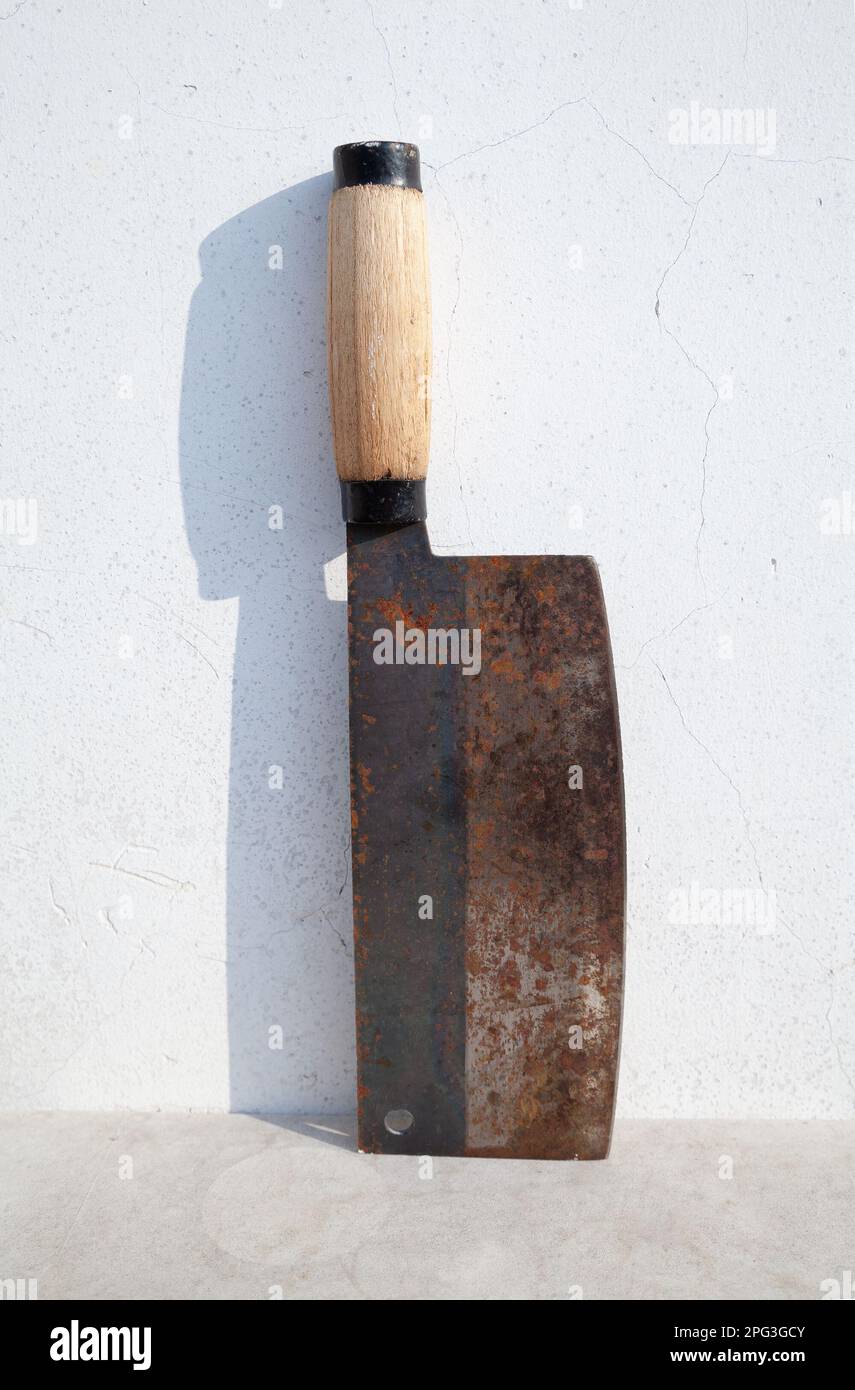 Old rusty Chinese cleaver leaning against a white wall. Large chopping