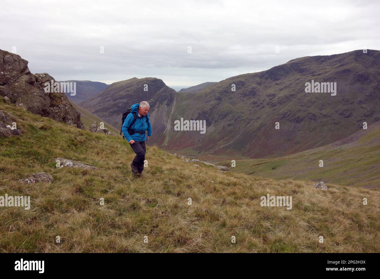 Man Walking to the Wainwright Pillar with Yewbarrow & Red Pike in the Background from the Top of the Black Sail Pass, Lake District National Park. Stock Photo