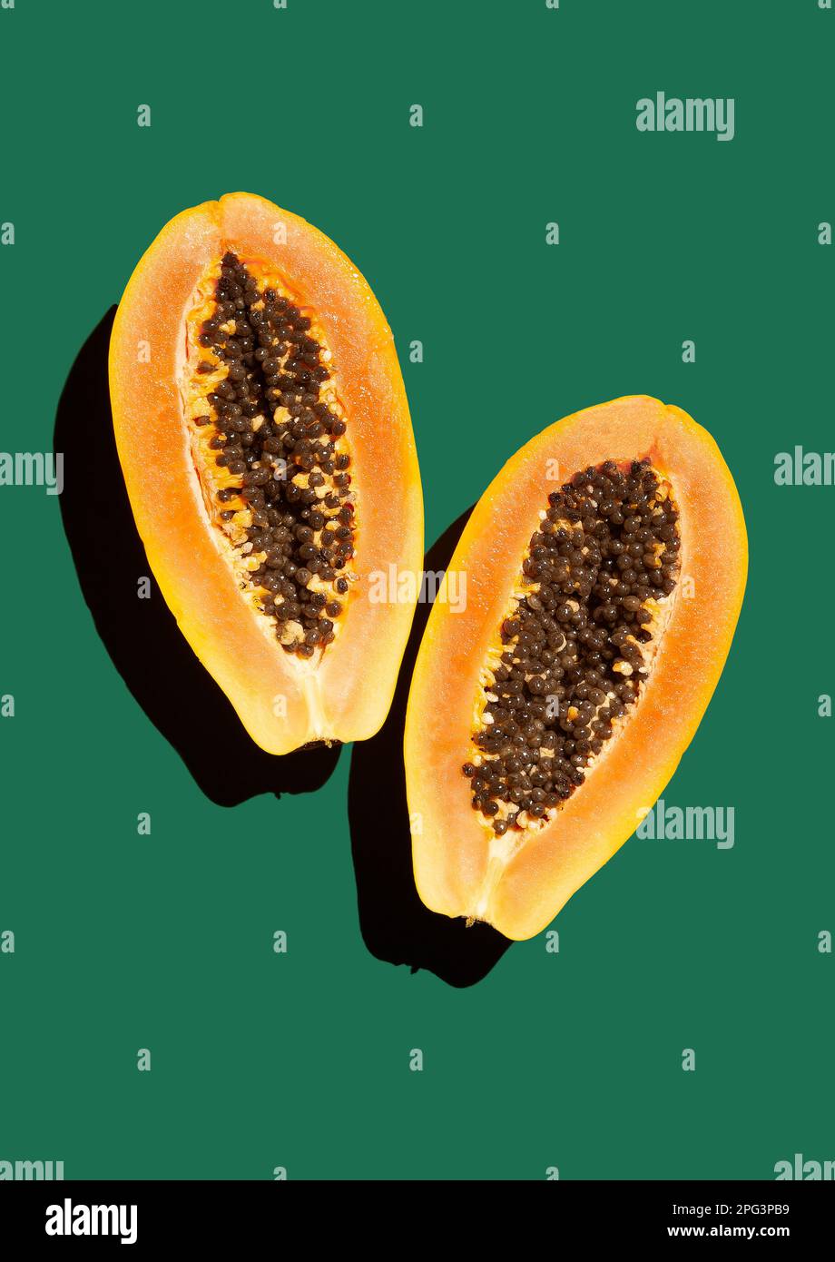 Ripe papaya in the cut, two halves on a green background, hard light ...