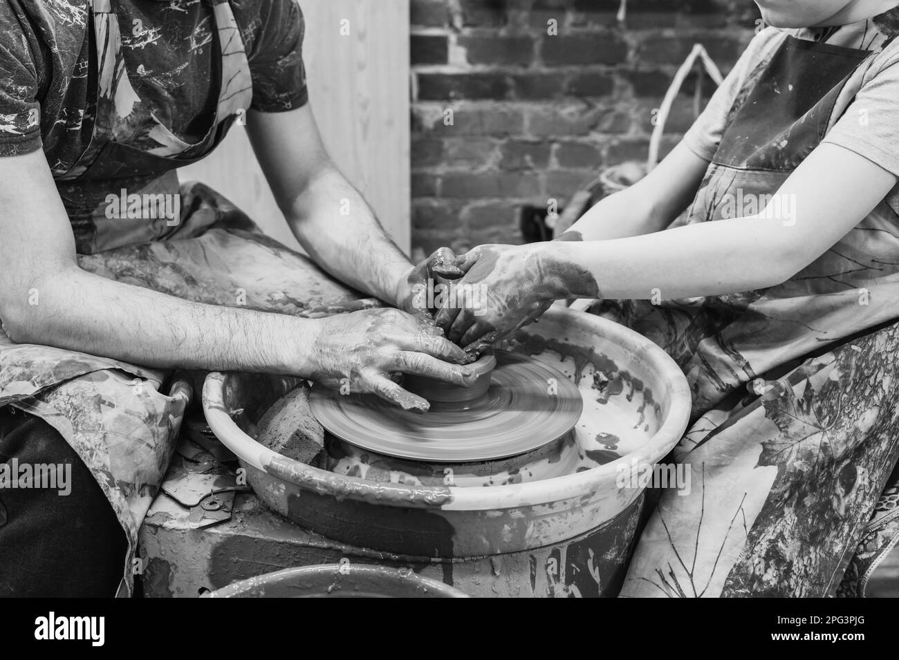 potter teaches the child. A craftsman sits on a bench with a potter's wheel and makes a clay pot. National craft. Black and white photo. Stock Photo