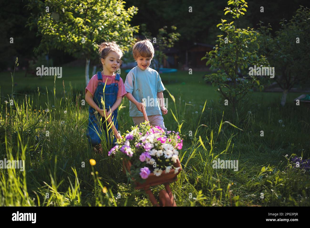 Little children with wooden wheelbarrow full of flowers Stock Photo - Alamy