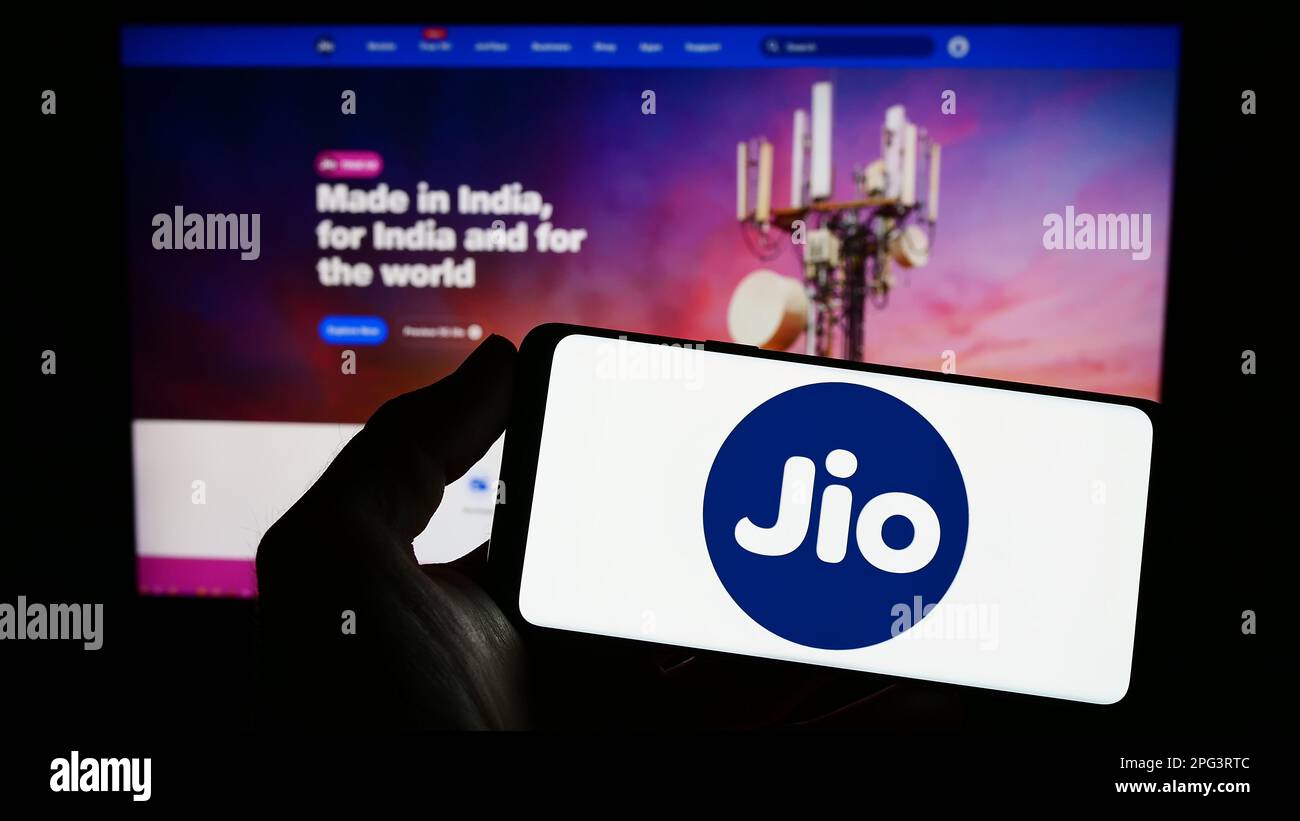 Person holding smartphone with logo of Indian telecommunications company Reliance Jio on screen in front of website. Focus on phone display. Stock Photo